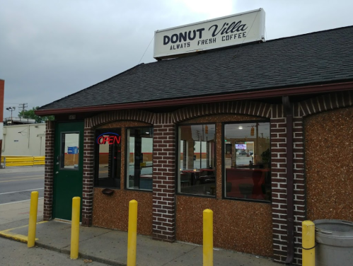 Exterior of Donut Villa, a small coffee shop with a sign that says "Always Fresh Coffee" and an "Open" neon light.