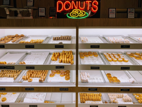 A display case filled with various donuts, labeled by flavor, under a glowing "DONUTS" sign.