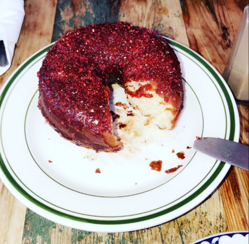 A partially eaten donut with red sprinkles on a plate, resting on a wooden table.