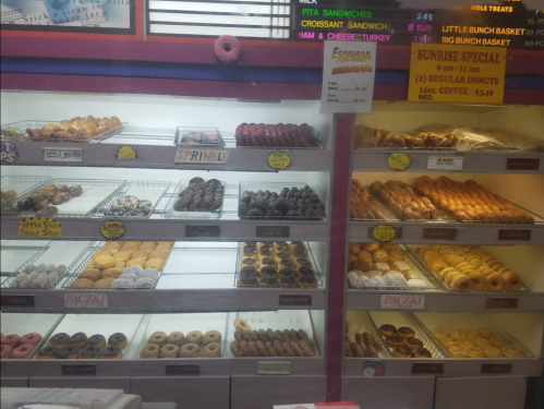 A display case filled with various donuts, including sprinkles, chocolate, and glazed options, with a menu sign above.