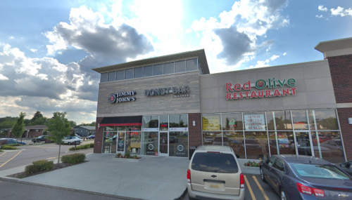 Exterior view of a shopping plaza featuring Jimmy John's, Donut Bar, and Red Olive Restaurant under a cloudy sky.