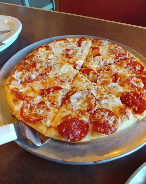 A freshly baked pepperoni pizza on a silver serving tray, sliced into eight pieces.