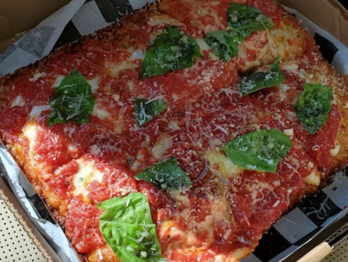 A rectangular pizza topped with tomato sauce, mozzarella cheese, and fresh basil leaves, in a pizza box.