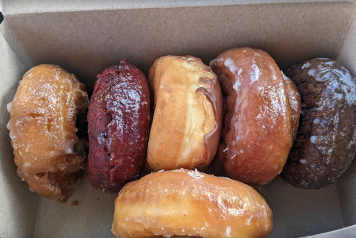 A box containing five assorted donuts with various glazes and colors, including red velvet and chocolate.