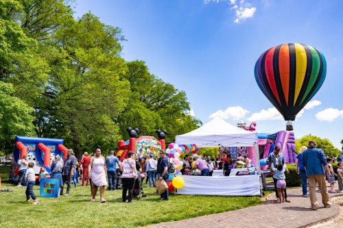 A vibrant outdoor festival scene with a hot air balloon, bounce houses, and families enjoying activities and colorful decorations.