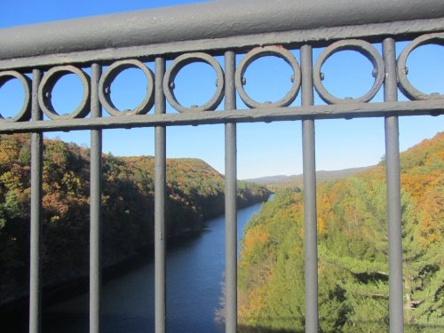 A view of a river winding through colorful autumn hills, framed by a decorative metal railing.
