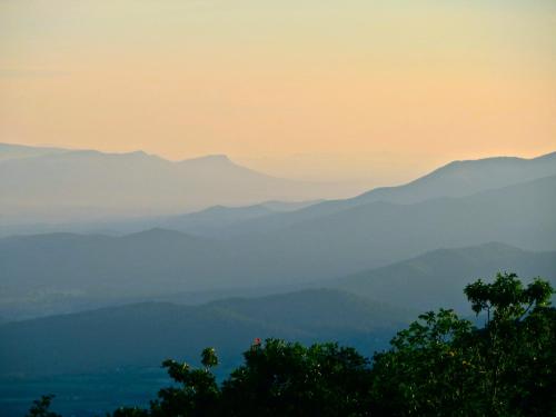 A serene landscape of layered mountains under a soft, hazy sky at sunset.
