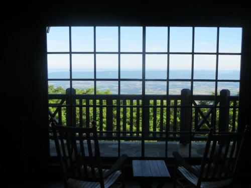 A scenic view from a cabin window, featuring rocking chairs and a vast landscape beyond.