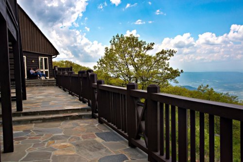 A scenic view from a wooden deck overlooking mountains and a blue sky with clouds.