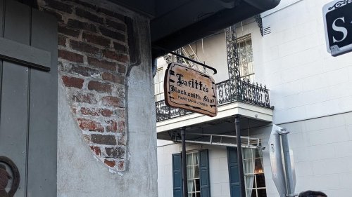 Sign for "Jean Lafitte's Blacksmith Shop" with a historic building and balcony in the background.