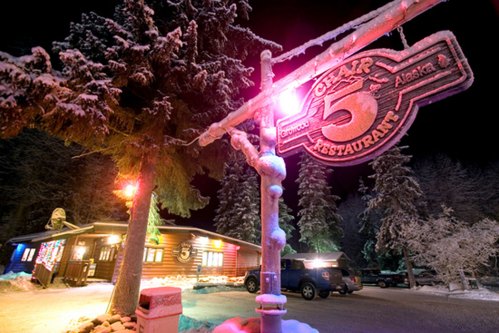 A snowy night scene featuring a lit restaurant sign for "5 Star Restaurant" surrounded by trees.