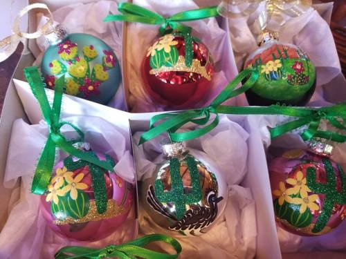 A box of six colorful Christmas ornaments, featuring floral and cactus designs, tied with green ribbons.
