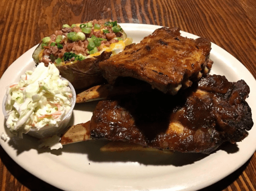 A plate featuring BBQ ribs, a loaded baked potato with toppings, and a side of coleslaw.