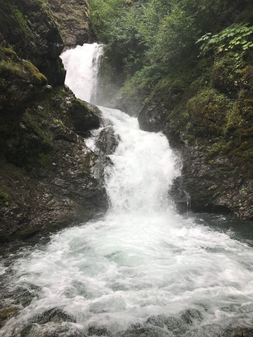 A cascading waterfall flows down rocky cliffs into a frothy pool, surrounded by lush greenery.