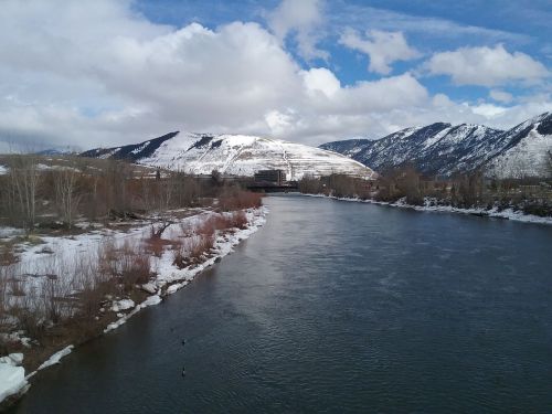 A river flows through a snowy landscape with mountains and clouds in the background.
