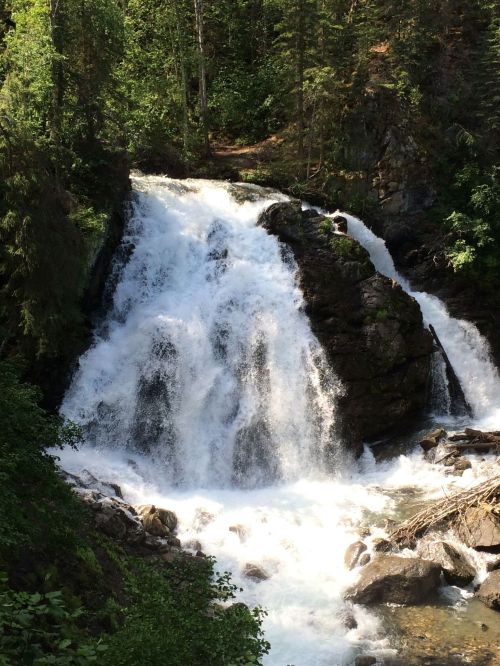 A cascading waterfall surrounded by lush green trees and rocky terrain, creating a serene natural scene.