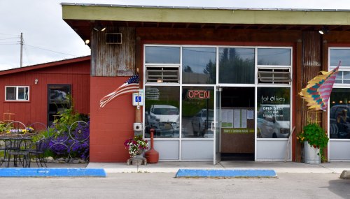 Exterior of a restaurant called "Fat Olives," featuring an open sign, colorful flags, and outdoor seating.