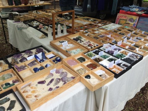 A display of various gemstones and crystals arranged in wooden trays on a table at an outdoor market.