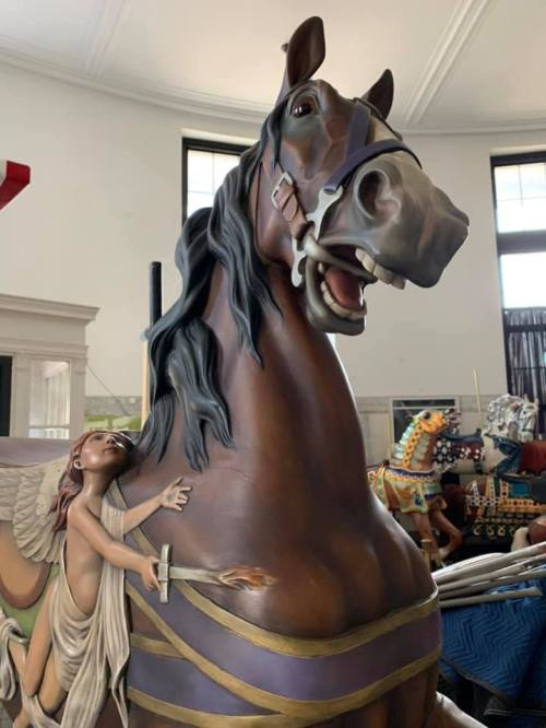 A detailed sculpture of a horse with a child angel holding a torch, set in a room with other carousel figures.