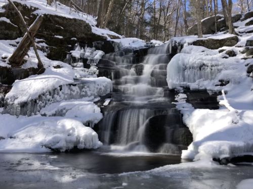A serene winter scene of a cascading waterfall surrounded by snow and ice in a forested area.