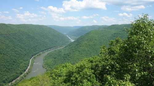 A scenic view of a winding river surrounded by lush green hills under a blue sky with fluffy clouds.