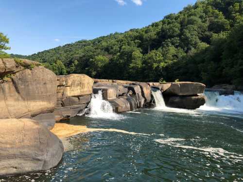 A serene river scene with cascading waterfalls and lush green hills in the background under a clear blue sky.