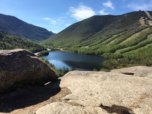 A scenic view of a tranquil lake surrounded by lush green mountains under a clear blue sky.