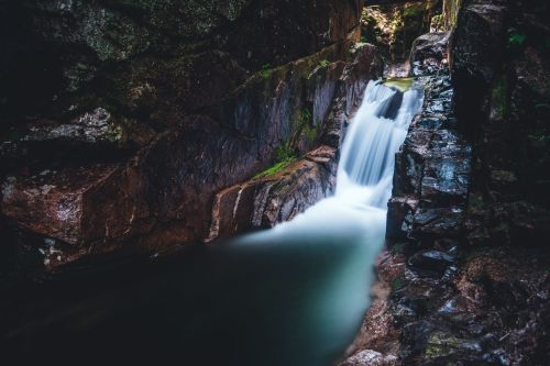 A serene waterfall cascading over smooth rocks in a dark, lush forest setting.