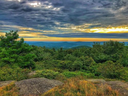 A scenic view of rolling hills and a colorful sunset, framed by lush greenery and rocky terrain.