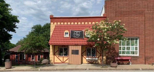 A charming building with a red-tiled roof, yellow walls, and a sign reading "Grace," surrounded by greenery.