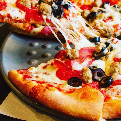 A close-up of a pizza with pepperoni, sausage, black olives, and melted cheese, with a slice being pulled away.