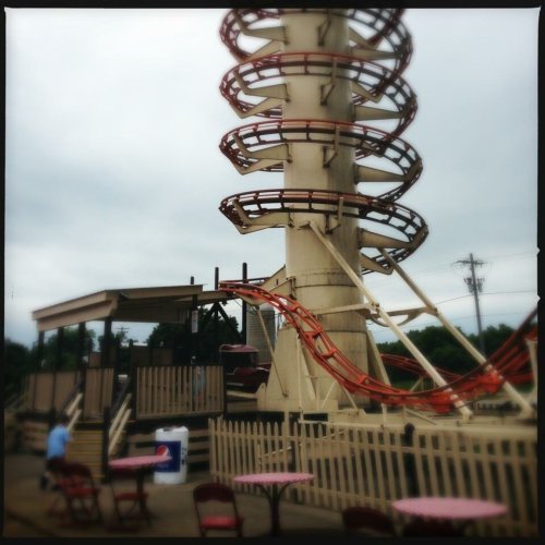 A tall water slide with a spiral design, surrounded by tables and a cloudy sky in the background.