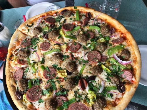 A large pizza topped with pepperoni, green peppers, onions, olives, meatballs, and herbs, served on a table.