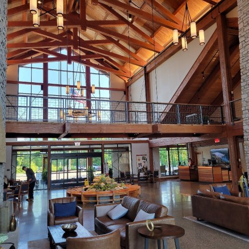Spacious lodge interior with high wooden ceilings, large windows, and cozy seating areas. Natural light floods the space.
