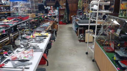 A cluttered aisle in a tool store, lined with various hand tools and equipment on tables and shelves.