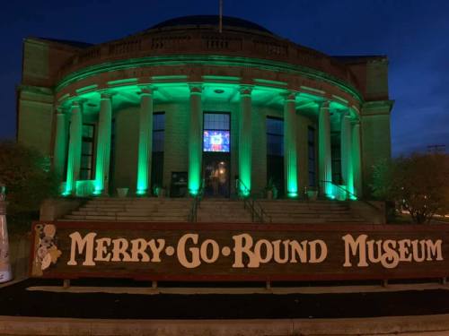 The Merry-Go-Round Museum illuminated in green at night, with a large sign in front.