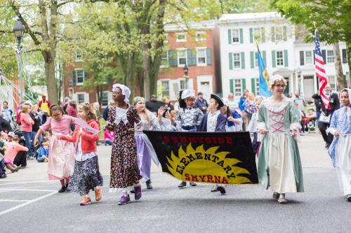 Children in historical costumes march in a parade, holding a banner for Sunnyside Elementary in Smyrna.