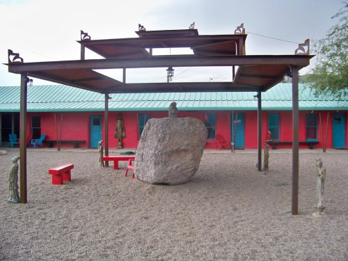 A unique outdoor space featuring a large rock, metal canopy, and colorful buildings with sculptures and seating.