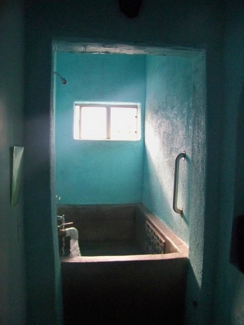 A dimly lit bathroom with turquoise walls, featuring a small window and a bathtub.