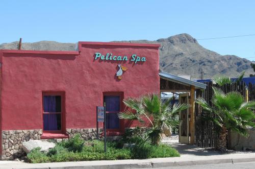 A colorful building labeled "Pelican Spa" with palm trees and mountains in the background under a clear blue sky.