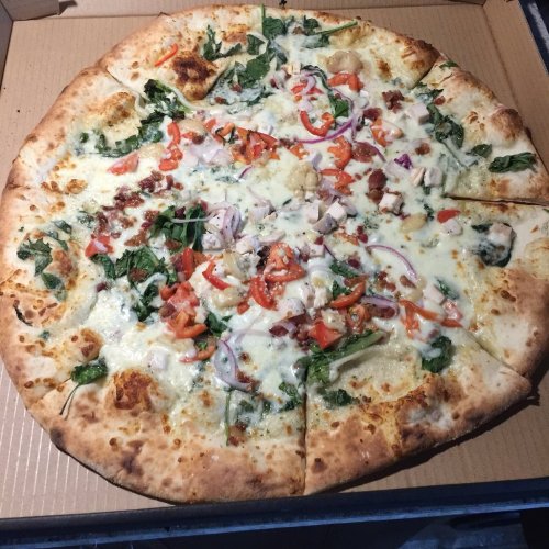 A large pizza topped with cheese, vegetables, and chicken, served in a cardboard box.