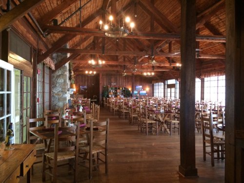 A spacious wooden dining hall with rows of tables and chairs, featuring rustic decor and warm lighting.