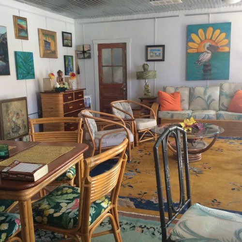 Cozy living room with tropical decor, rattan furniture, artwork on the walls, and a colorful rug.