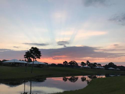 A serene sunset over a pond, with rays of light breaking through clouds and reflecting on the water.