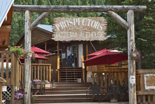 Sign for "Prospectors Pizzeria: Alehouse" at a rustic wooden building with outdoor seating and red umbrellas.