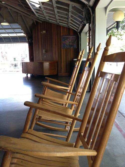 A row of wooden rocking chairs in a spacious, well-lit interior with wooden walls and a large window.