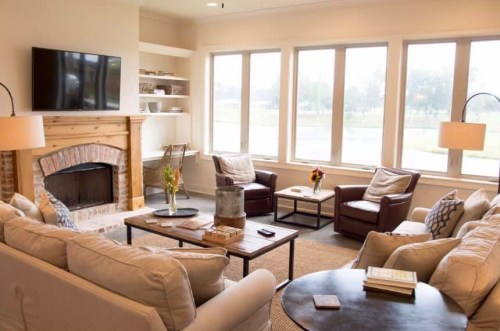 Cozy living room with a fireplace, large windows, comfortable seating, and a coffee table adorned with books and flowers.