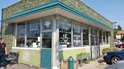A green brick building with large windows, featuring a sign for a market and a person walking by.