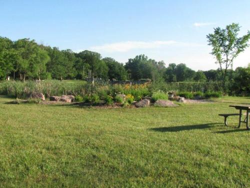 A serene park scene featuring a grassy area, a flower garden with rocks, and trees in the background under a clear sky.