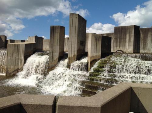 A concrete structure with cascading water flows over steps, under a blue sky with scattered clouds.